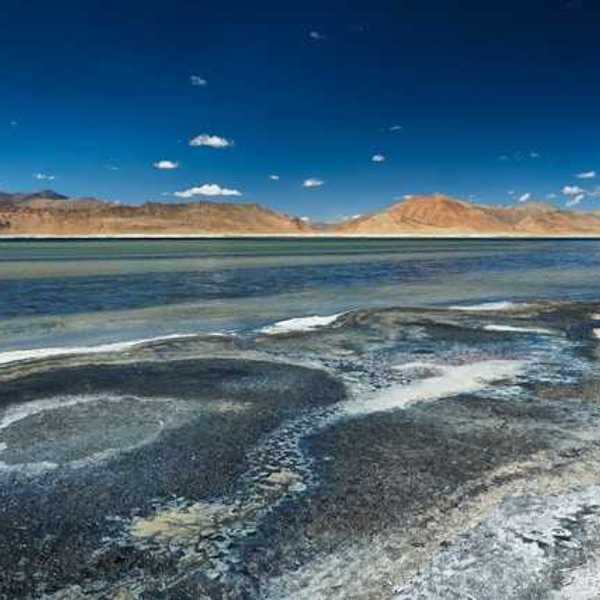 Salt flats in front of a lake with mountains in the distance