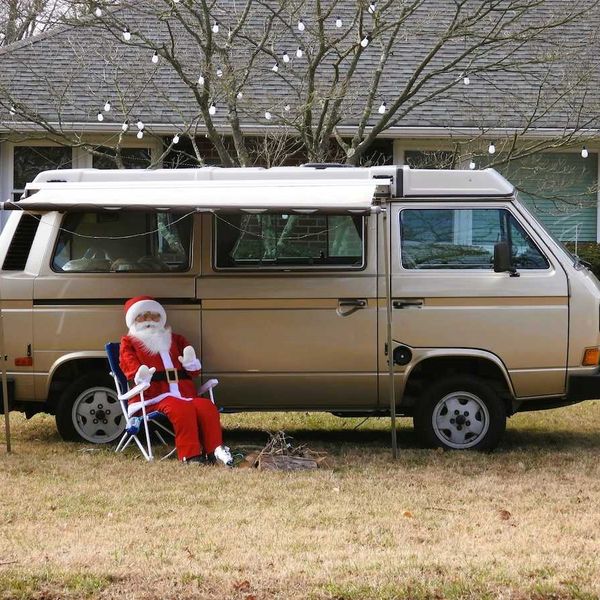 'Santa Claus' sitting in lawn chair adjacent to a camper van on snowless lawn