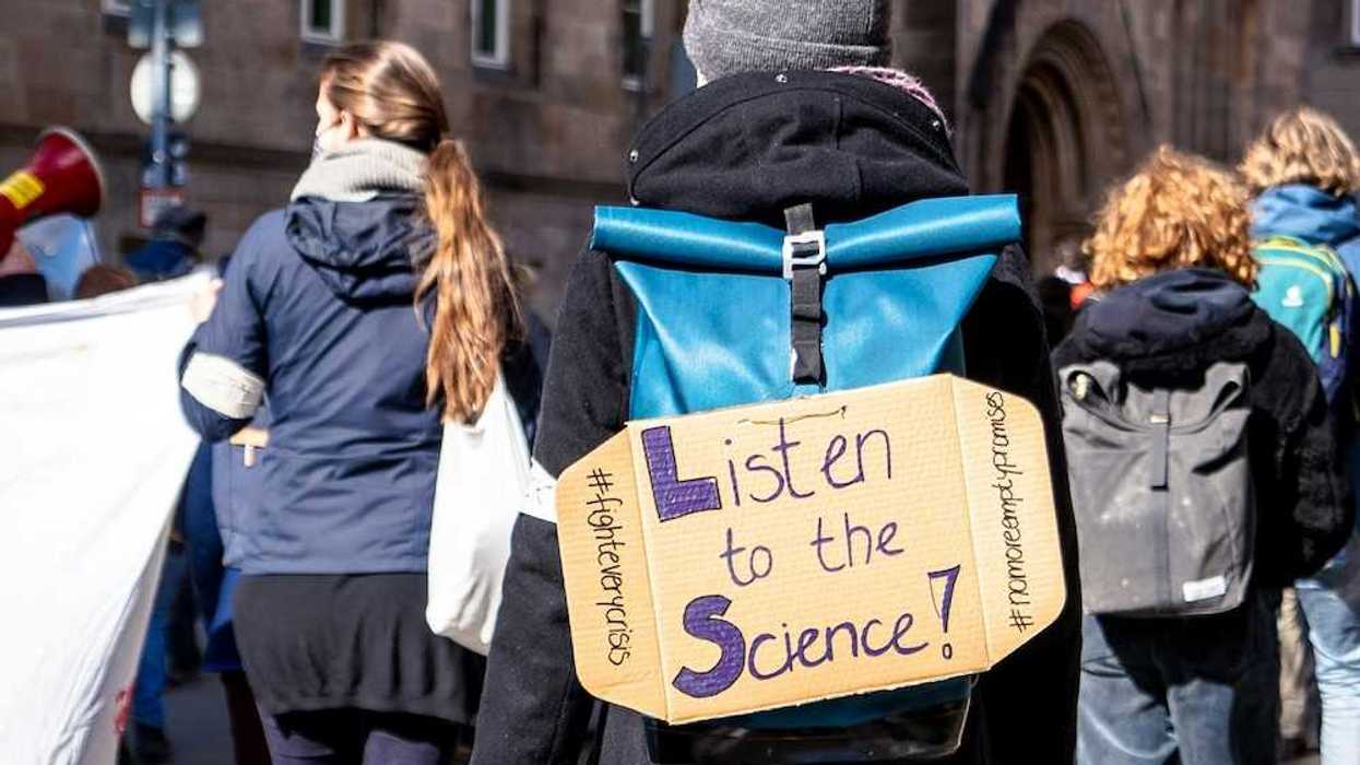 School children march for science with sign on backpack reading "Listen to the Science!"