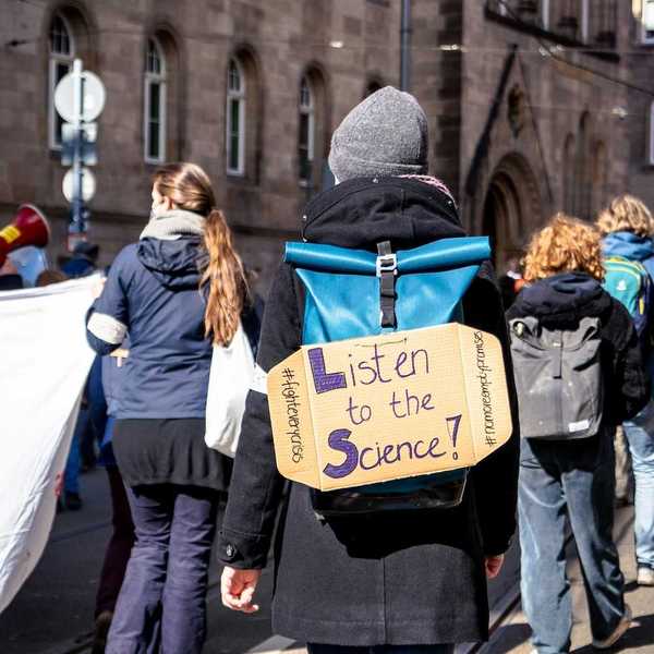School children march for science with sign on backpack reading "Listen to the Science!"