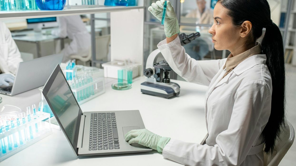 Scientist scrutinizes test tube in right hand and left hand on laptop computer