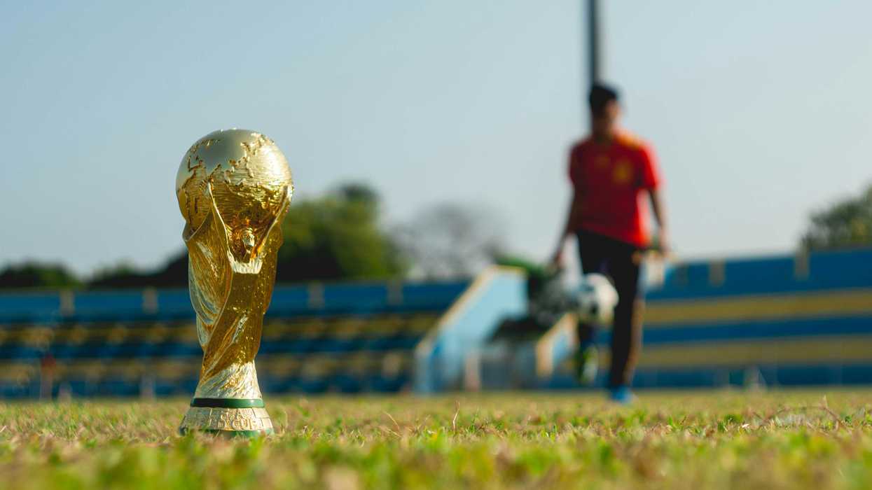 selective focus photography of gold-colored trophy on grass field during daytime with soccer player in background.