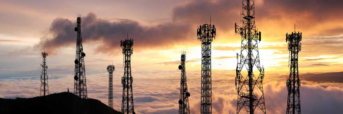 Several cell towers on top of a hill at sunset