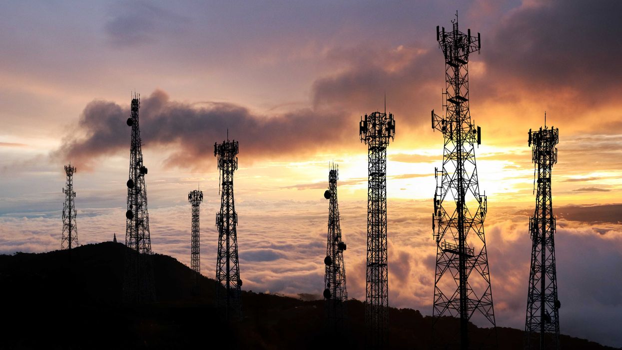 Several cell towers on top of a hill at sunset