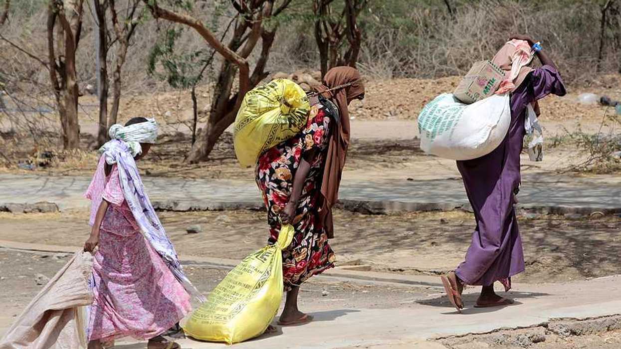 Several Somalian women carry bags of food at an African refugee camp