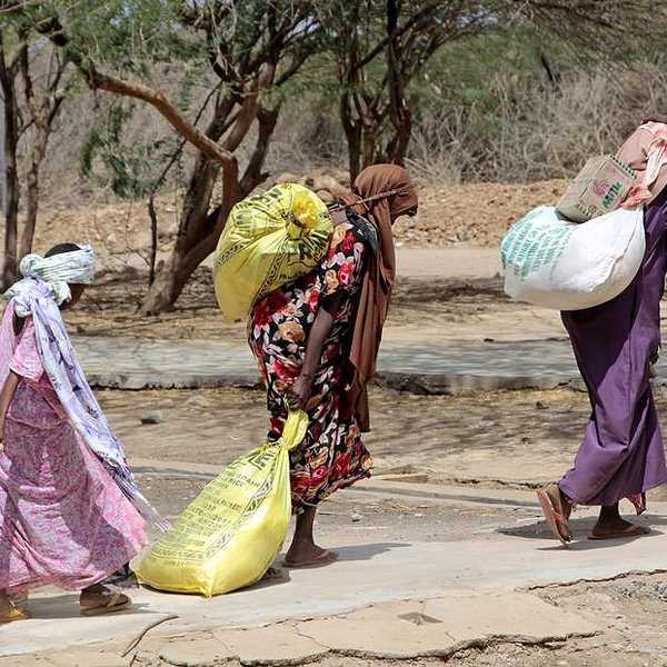 Several Somalian women carry bags of food at an African refugee camp
