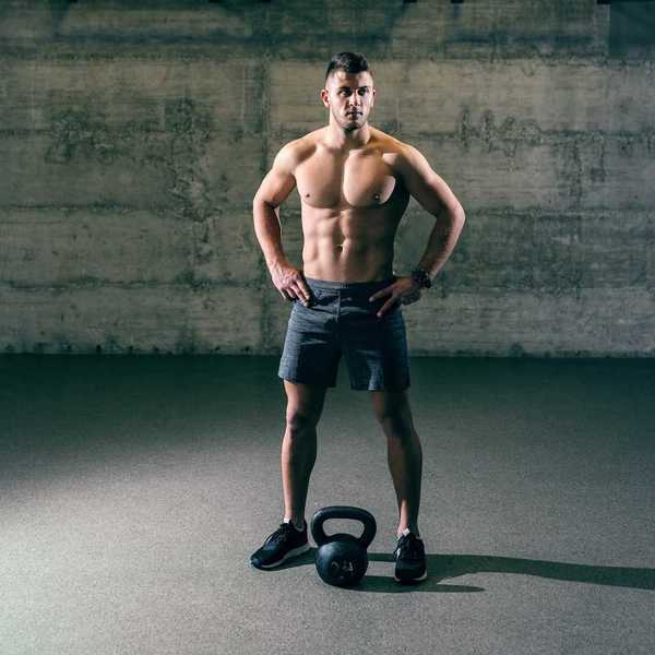 Shirtless man in athletic shorts standing over kettle ball