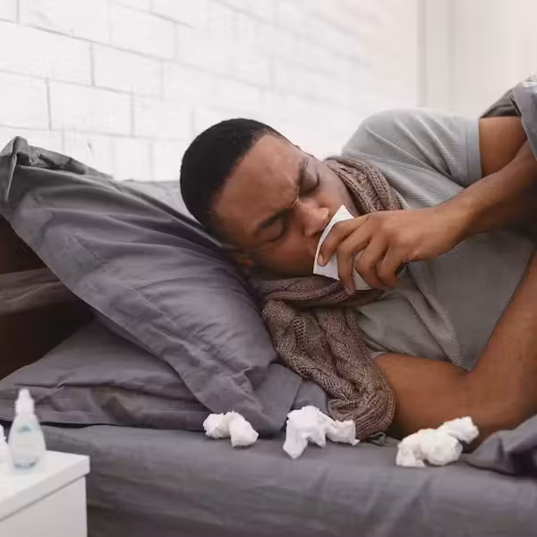 Sick African American man coughing holding paper napkin near mouth suffering from respiratory ailment