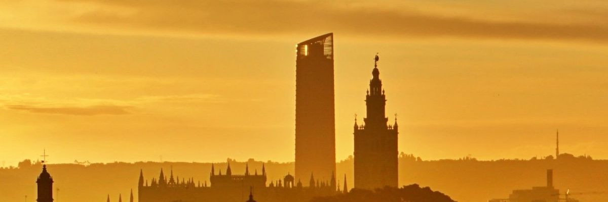 silhouette of buildings in Seville, Spain against a golden evening sky.