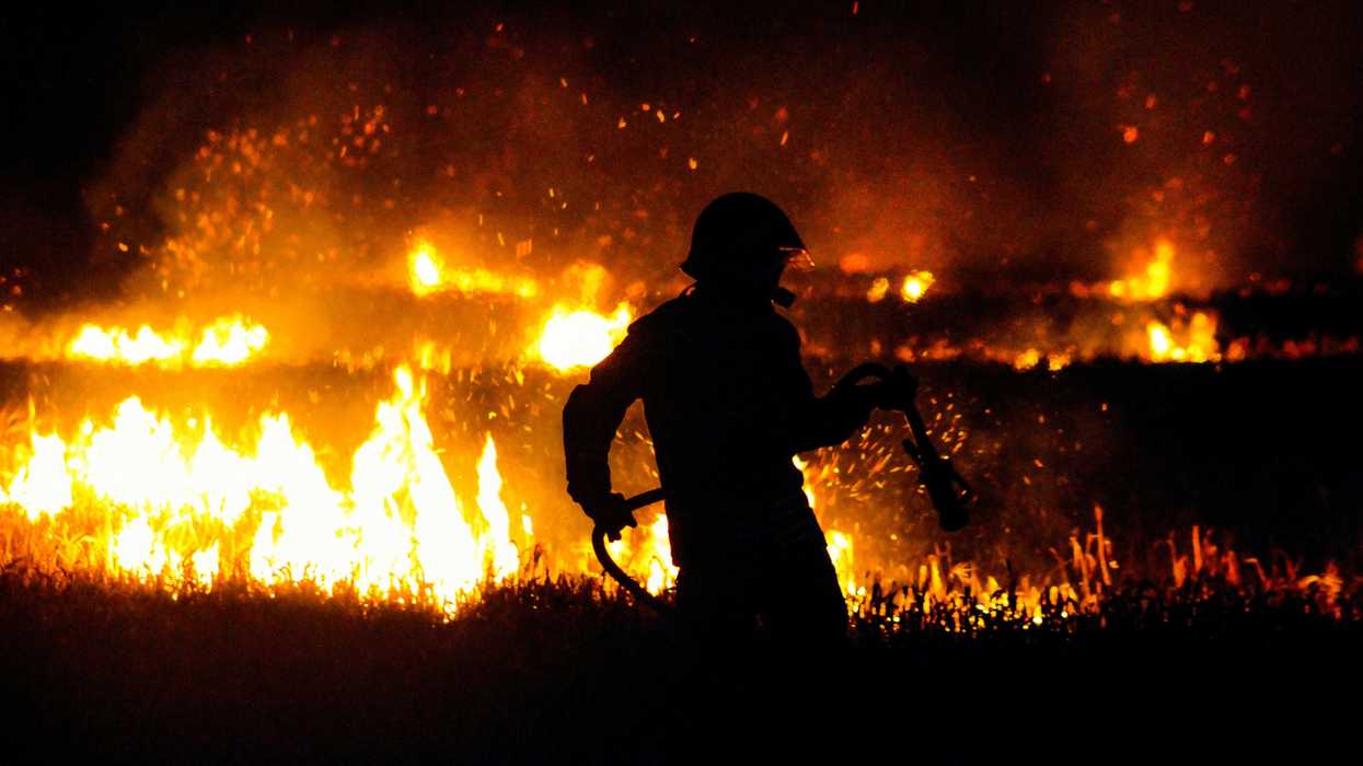 silhouette of firefighter standing on edge of wildfire during night time.