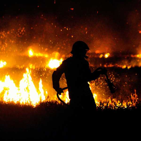 silhouette of firefighter standing on edge of wildfire during night time.