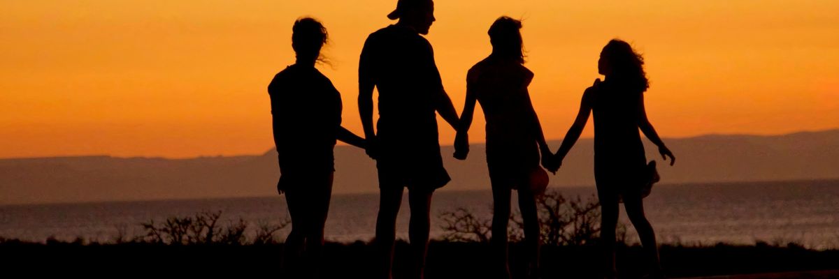 silhouette of people holding hands by a lake at sunset