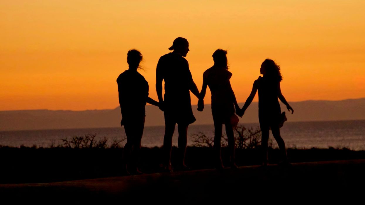 silhouette of people holding hands by a lake at sunset