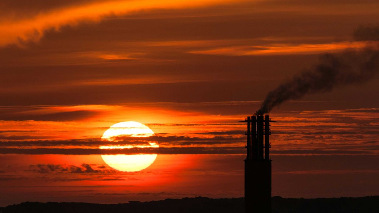 Silhouetted smokestacks against an orange sunset.