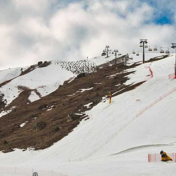 Ski lift on a partially snowy mountain with snowmaking equipment