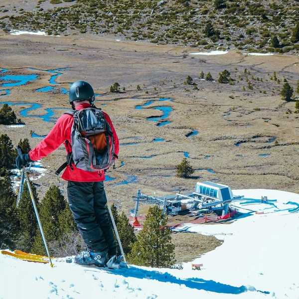 Skier in red jacket poised to descend to lift station. Spotty snow cover.