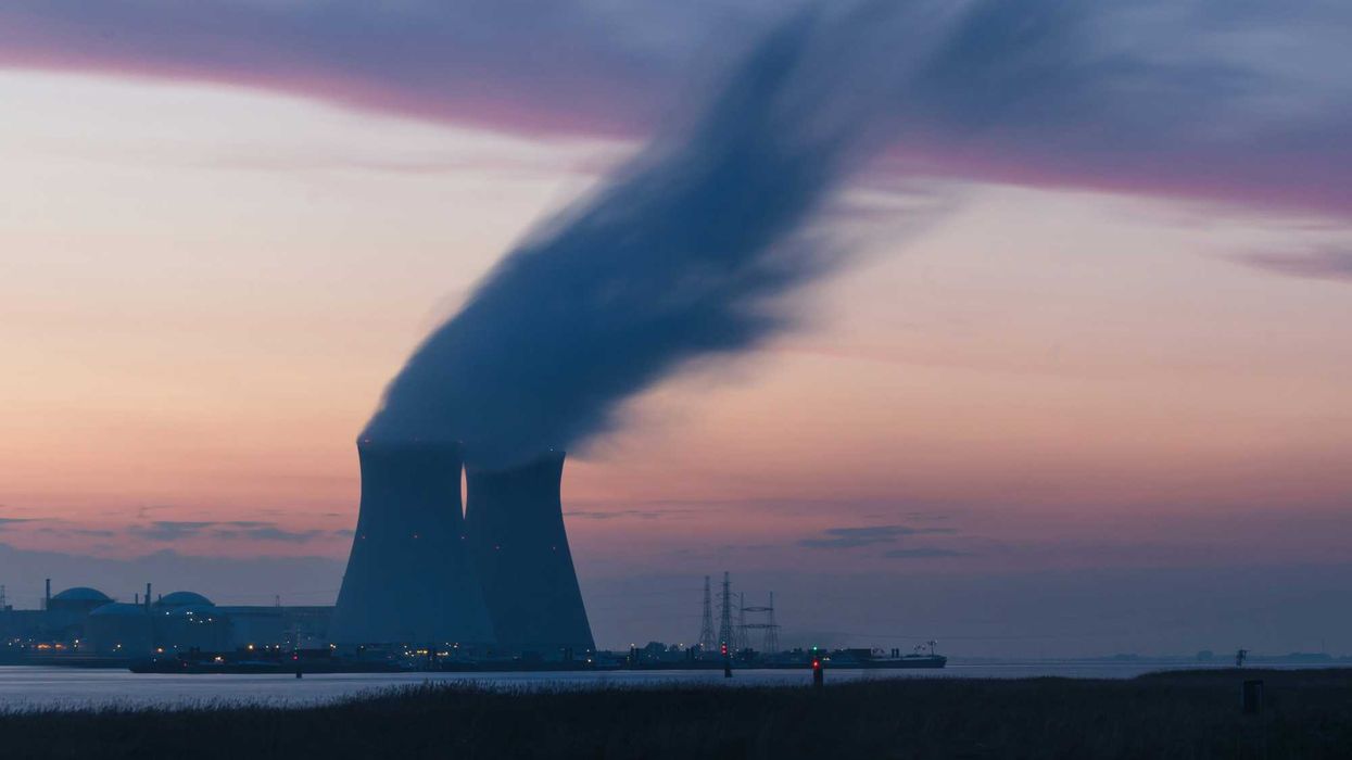 skyline photography of nuclear plant cooling tower blowing smokes under white and orange sky at daytime.