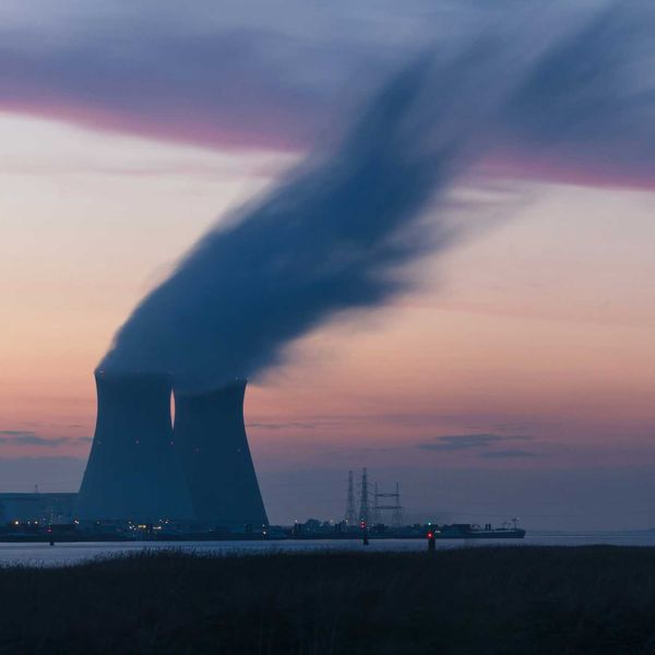 skyline photography of nuclear plant cooling tower blowing smokes under white and orange sky at daytime.