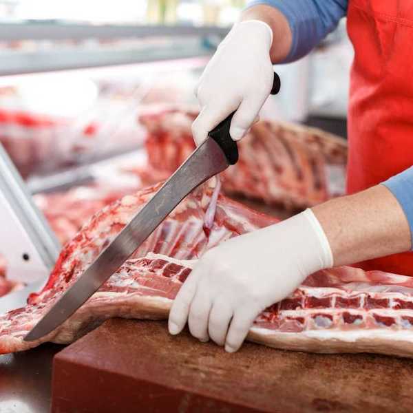 Slaughterhouse worker processing meat with a large knife