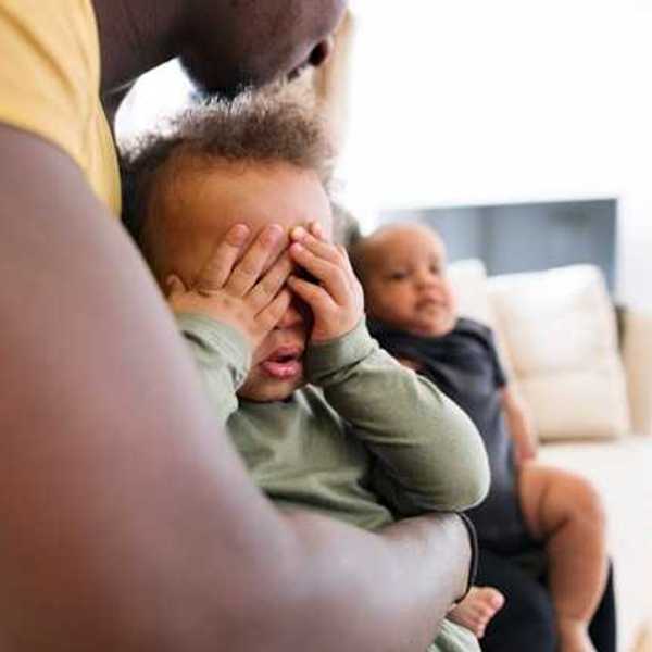 Small Black child sitting his fathers lap covering his eyes