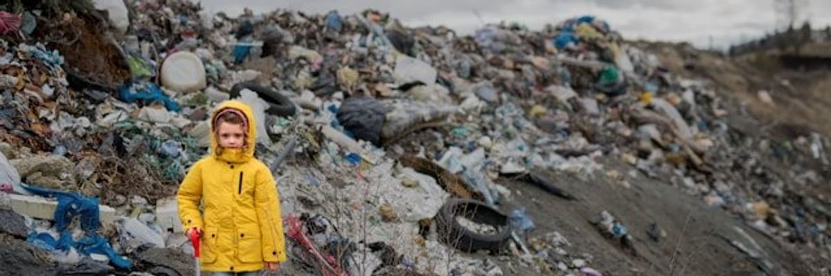 Small child with trash pickup tools standing in front of a large pile of waste.