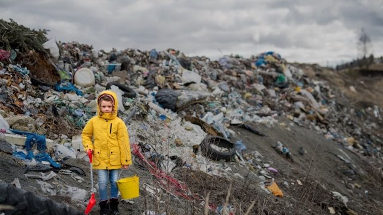 Small child with trash pickup tools standing in front of a large pile of waste.