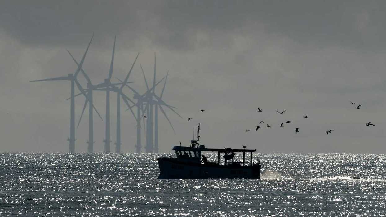 Small fishing boat trailed by sea birds with wind turbines in the background.