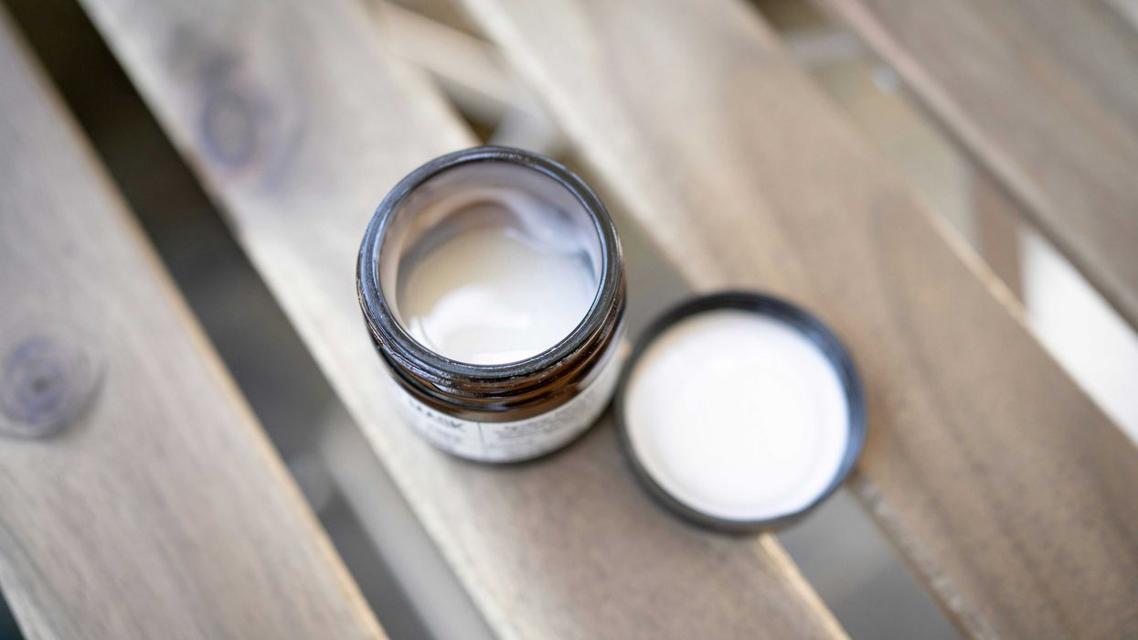 Small jar of lotion with lid off on a wooden table.