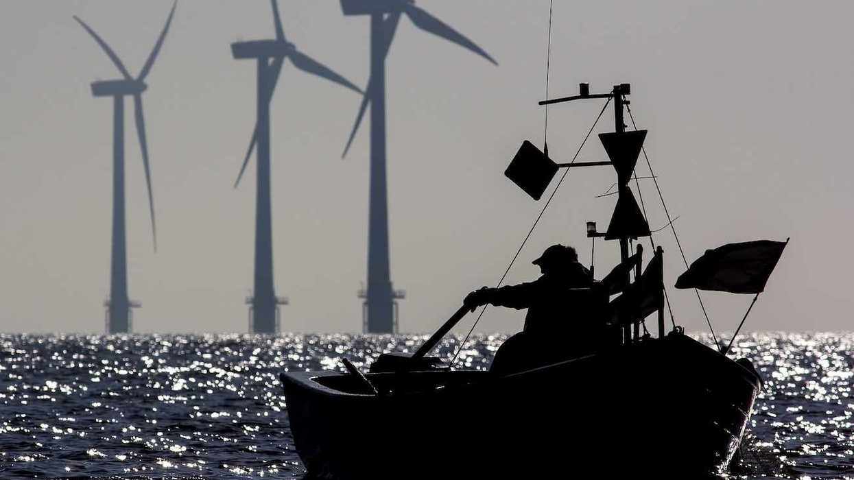 Small one-man fishing boat silhouetted at sunrise with sustainable energy wind turbines in the background.