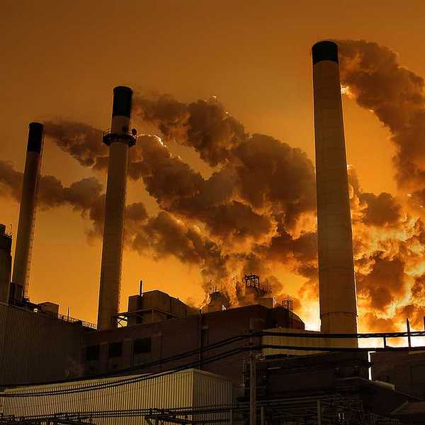 Smoke billowing out of smokestacks against an orange sky