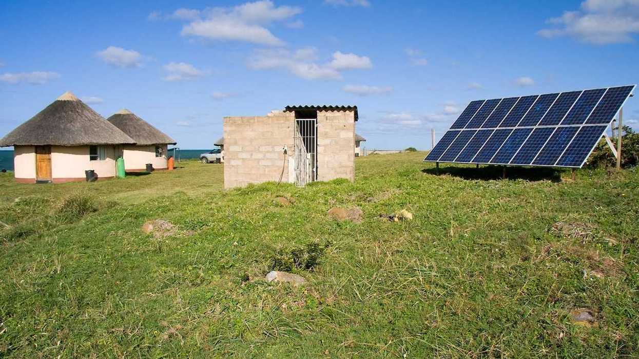 Solar panel providing power to a rural area in Africa. Detached array powering two thatched-roof buildings.