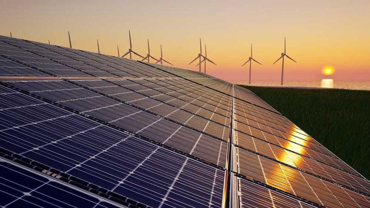 Solar panels in foreground with wind turbines and a setting (or rising) sun in background