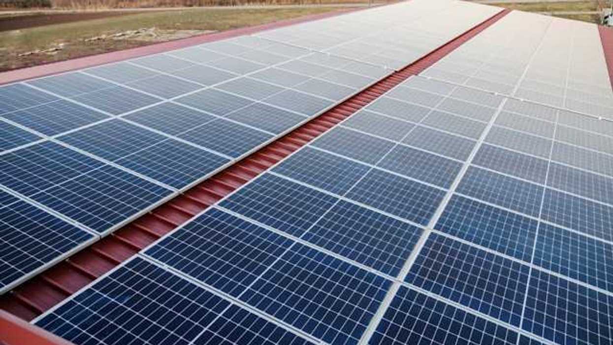 Solar panels on a red metal roof with a green landscape in the background