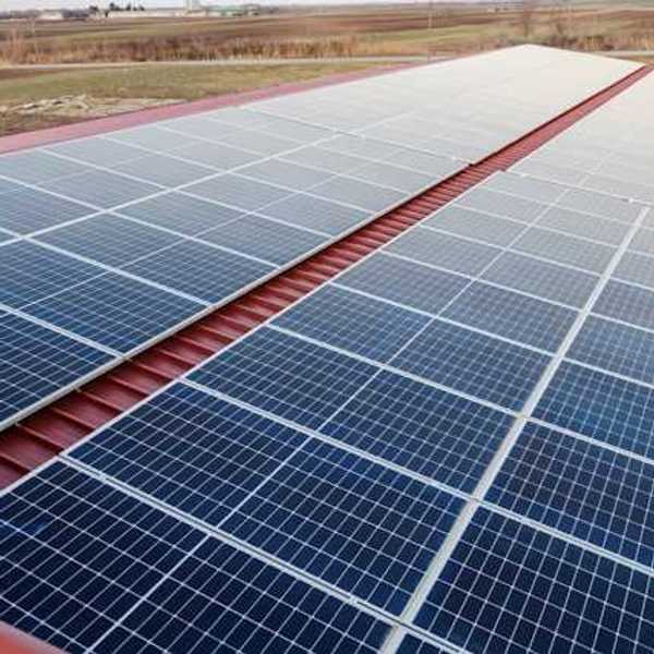 Solar panels on a red metal roof with a green landscape in the background