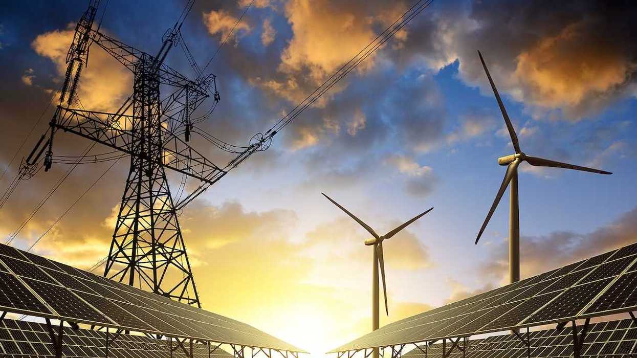 Solar panels with wind turbines beneath electrical transmission lines at sunset.