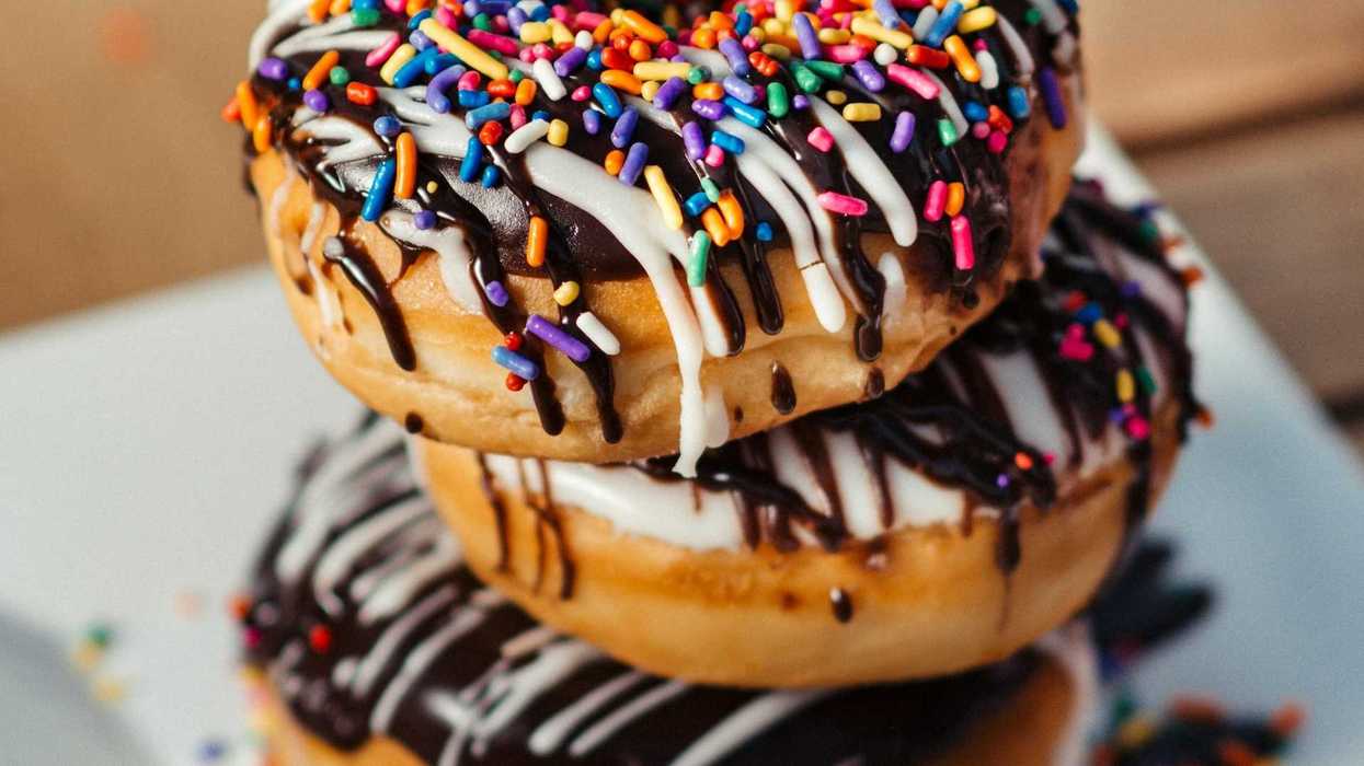 Stack of three donuts laden with chocolate, sugary icing, and multicolored sprinkles