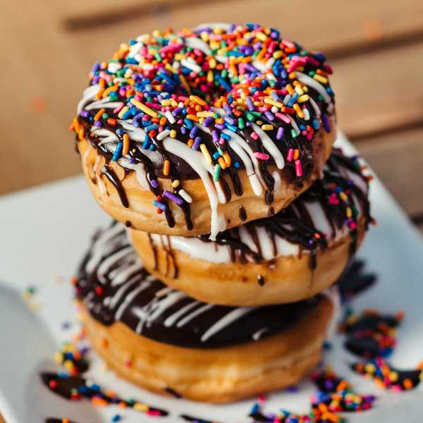 Stack of three donuts laden with chocolate, sugary icing, and multicolored sprinkles
