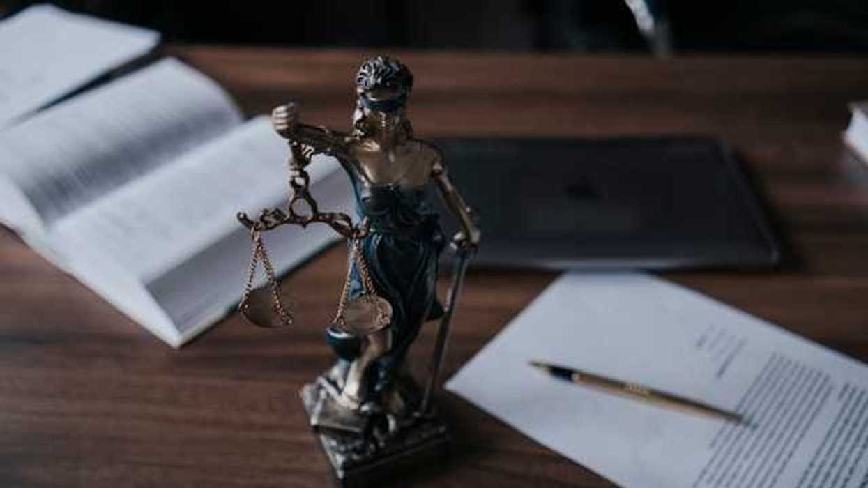 Statue of lady justice on a wooden desk with legal manuals and documents nearby