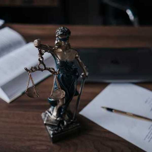 Statue of lady justice on a wooden desk with legal manuals and documents nearby