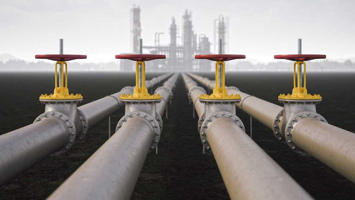 Steel quad-pipeline in the foreground with yellow/red valves, leading to a reinery in the background