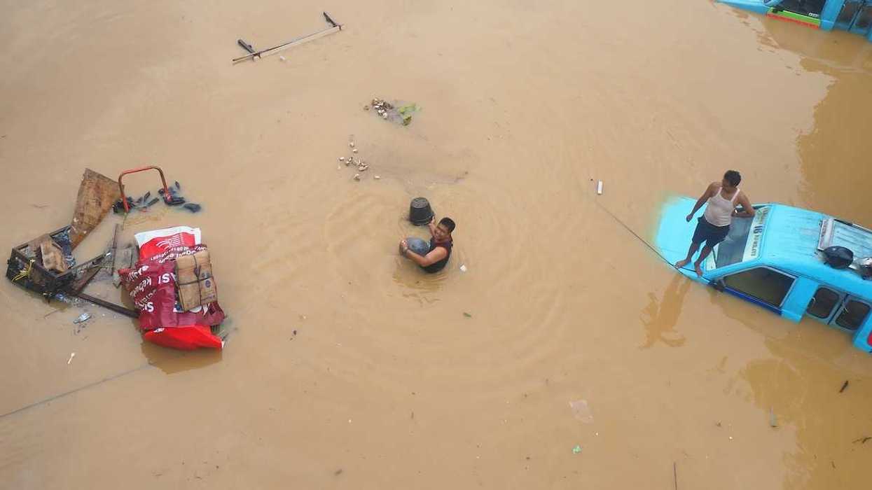 Submerged street in Jakarta, Indonesia with two blue vehicles submerged to their windows - one with a man on the hood.