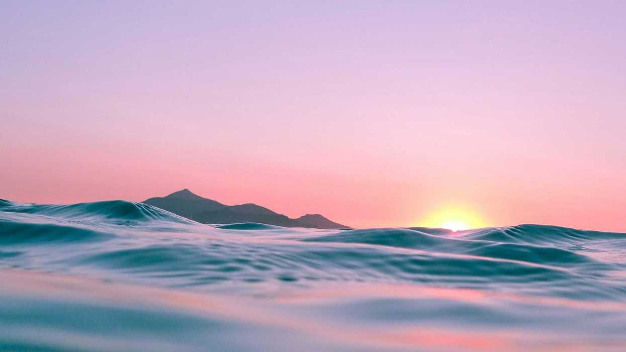 Sun rising over ocean waters casting pink hue over water and sky.