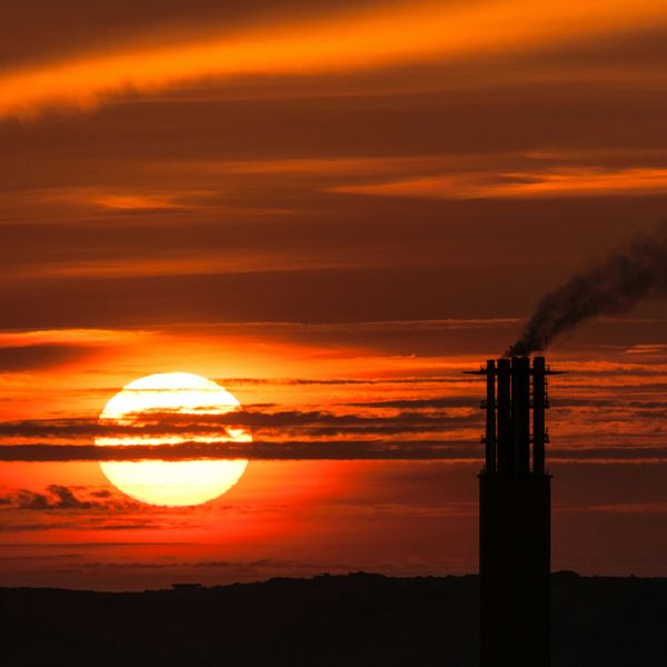 Sun setting behind a power plant smoke stack emitting pollution