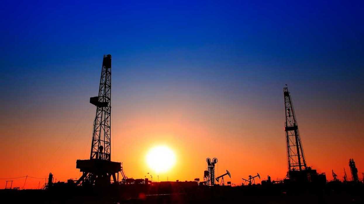 Sun setting over oilfield - drilling rigs and pumpjacks silhouetted against sunset sky.