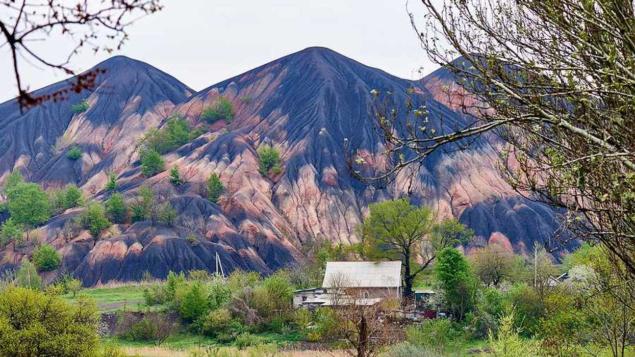 Tall slag heaps in the distance with green fields and trees in the foreground