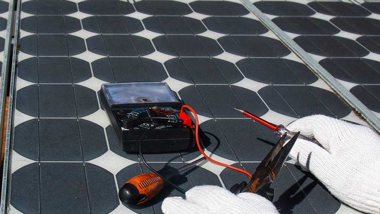 Technician wearing white gloves testing solar panel with multimeter