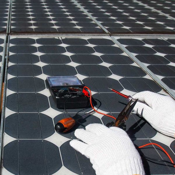 Technician wearing white gloves testing solar panel with multimeter