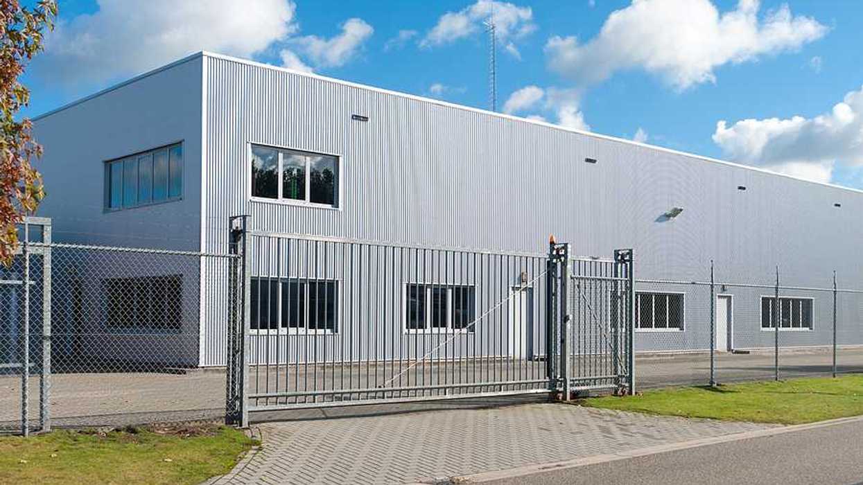 The exterior of a gray warehouse-type building behind a fence