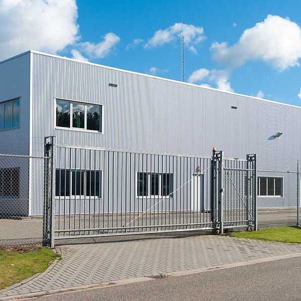 The exterior of a gray warehouse-type building behind a fence
