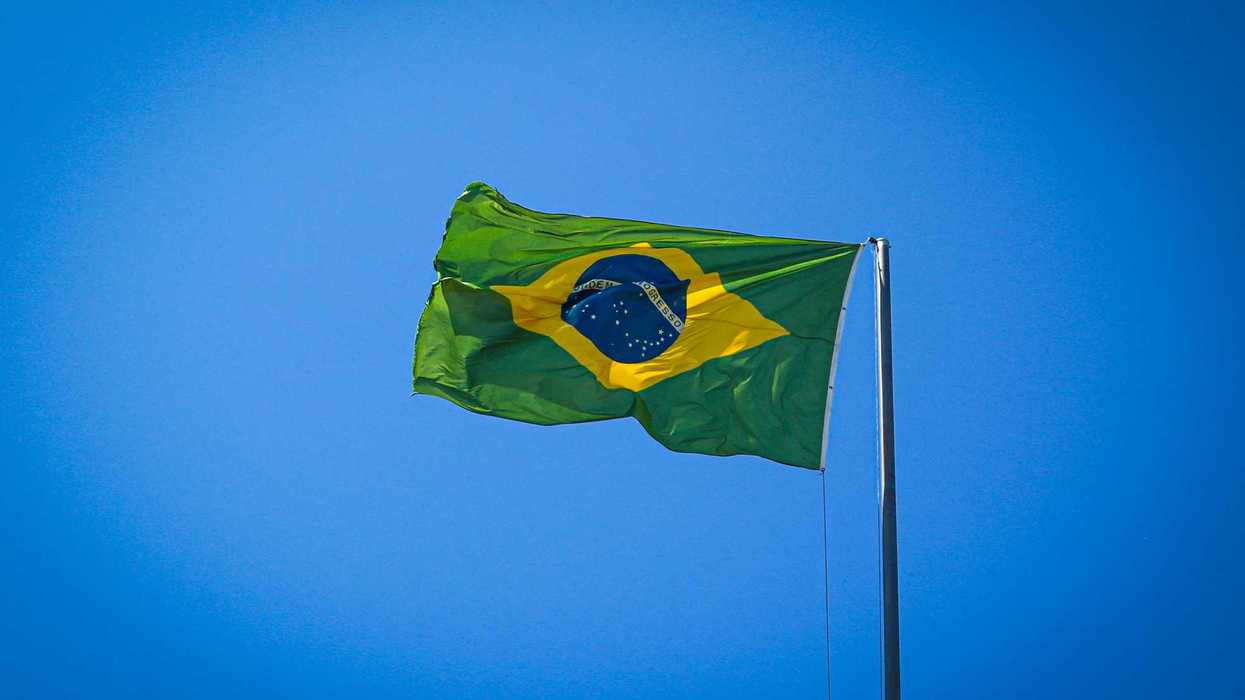 The flag of Brazil waving on a pole against a clear blue sky.